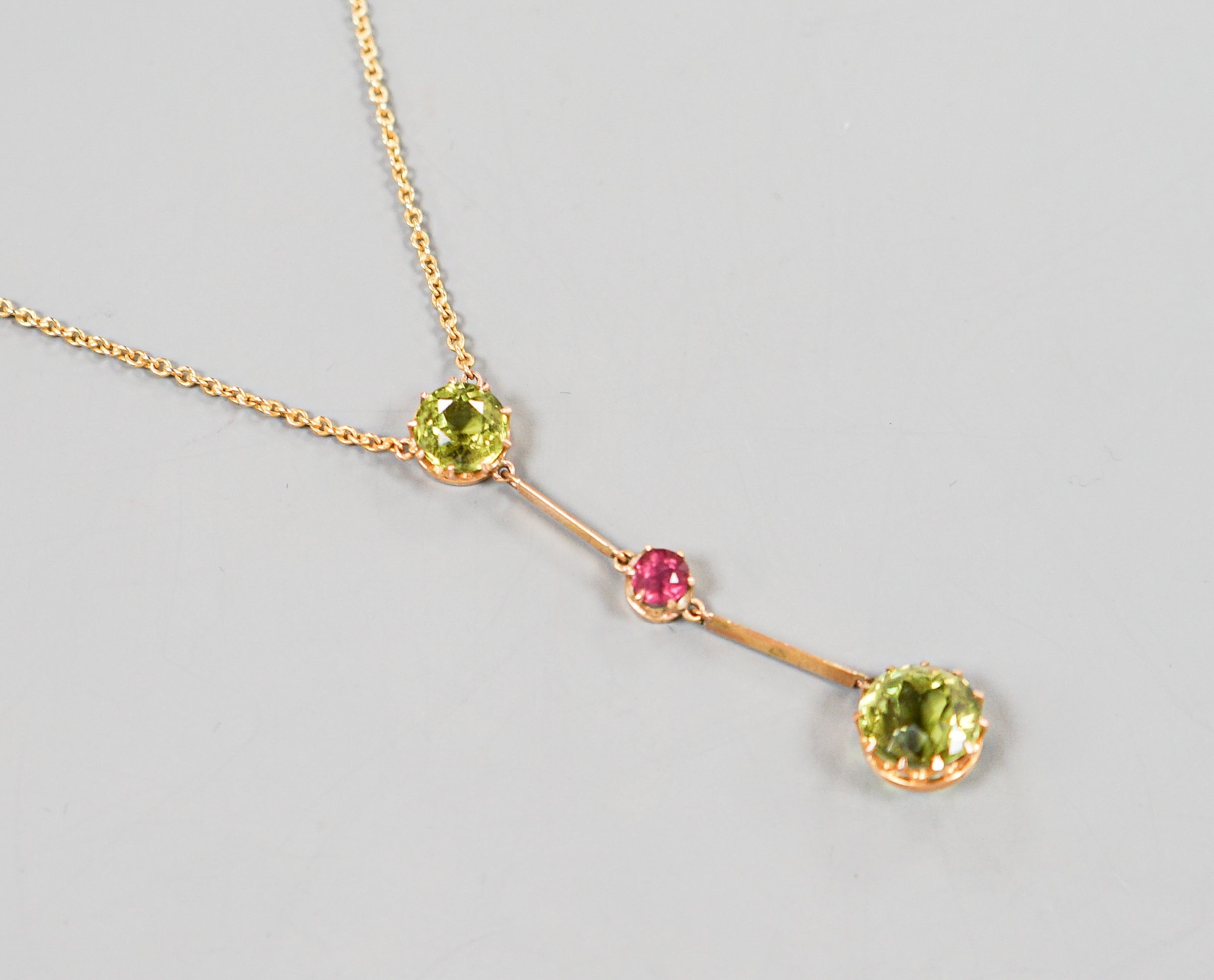 A 20th century yellow metal, two stone peridot and single stone pink tourmaline? set drop line pendant necklace, 51cm, gross 5.5 grams.